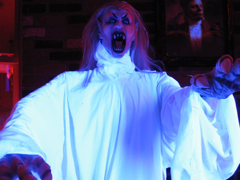 This is my new glowing vampire.  She was a severed head I bought on sale after Halloween last year, but I have plenty of heads hanging, so I made her a porch-creature.  I outfitted her in robes I stitched out of cotton fabric I got for seven bucks (ten yards), and put her under a 48" blacklight I bought at Spirit last year during the after Halloween sale.  Under her robes, she's a pvc frame attached to a weighted wood base I built.